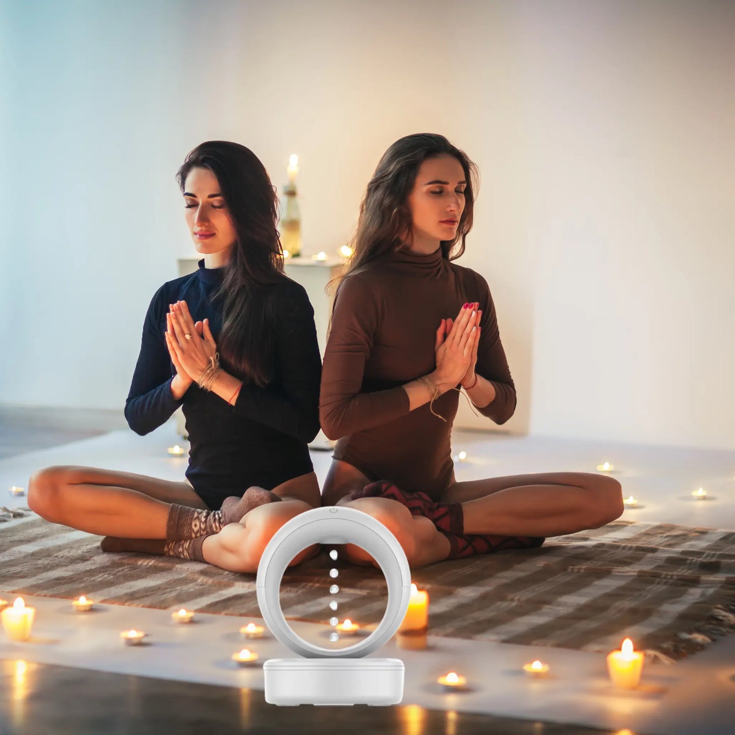 Twee vrouwen mediteren in een serene sfeer met een NUVIA lucht diffuser en kaarslicht.