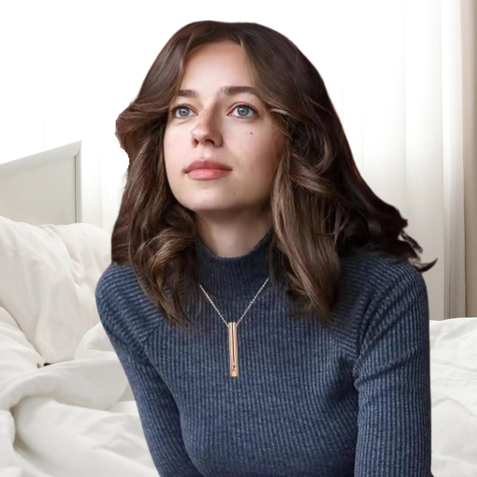 Woman wearing a RESPIRA breathing tool pendant, looking serene and relaxed in a cozy bedroom setting.