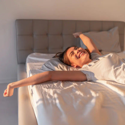 Vrouw geniet van een goede nachtrust op een bed met NEURA-kussen, omringd door rustgevende ochtendlicht.